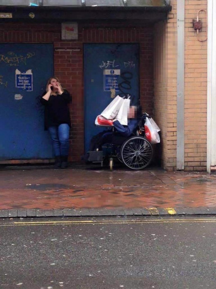 Support Worker Takes A Smoke Break With Shopping Bags Stacked On Her Wheelchair-Bound Patient